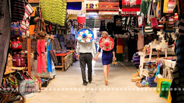 Connie Hanks Photography // ClickyChickCreates.com // engagement couple session, Rosarito, Mexico, mercado, market, colorful, turquoise, blue, gray, wood, wheel, rustic, arches, archways, kiss, sombreros